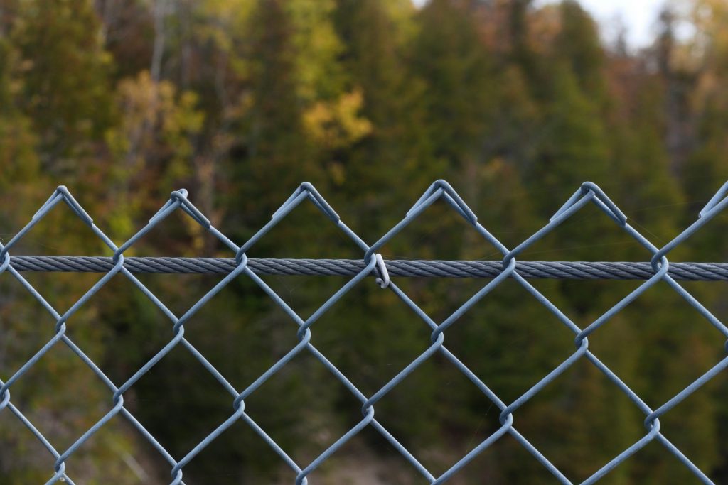 a close up of a chain link fence with trees in the background